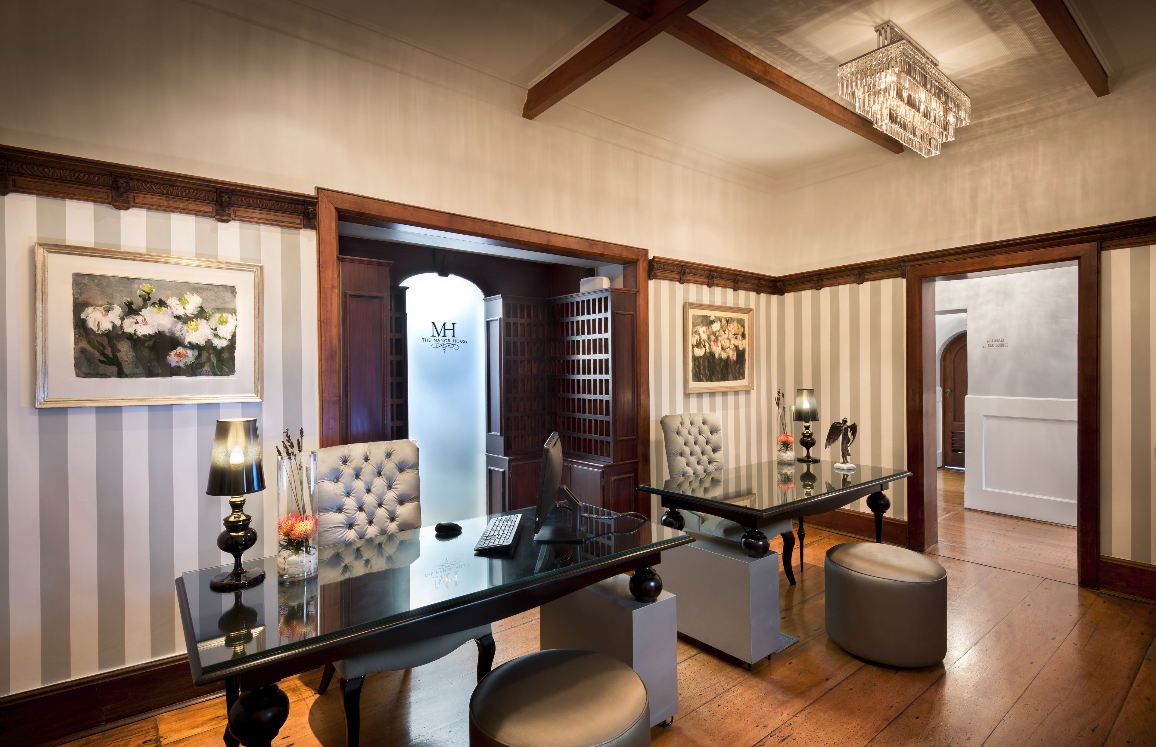 A modern hotel lobby with a glass table, two chairs, a chandelier, and framed artwork on the walls.