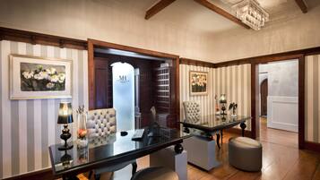 A modern hotel lobby with a glass table, two chairs, a chandelier, and framed artwork on the walls.