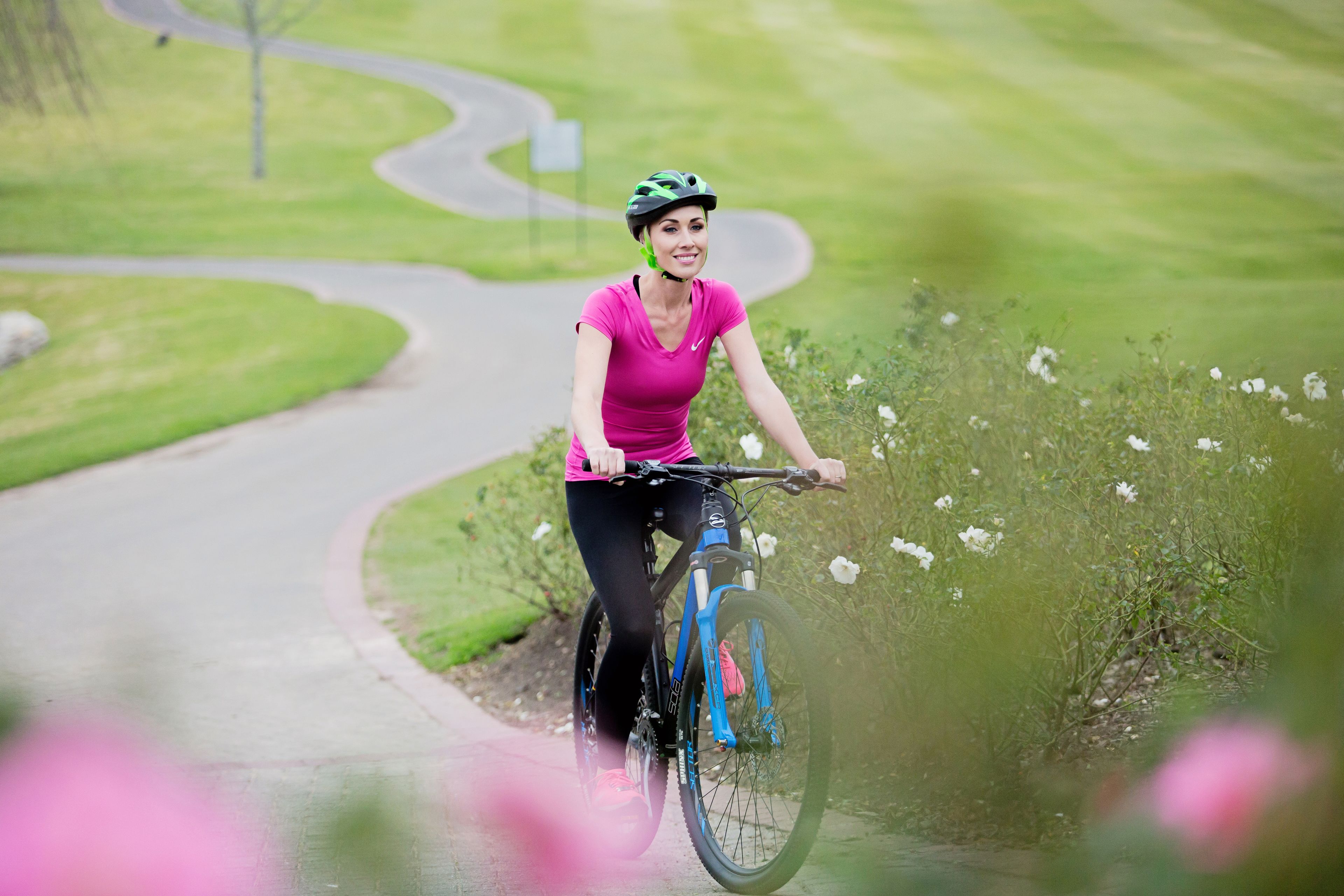 A person riding a bicycle on a paved path surrounded by greenery and flowers.