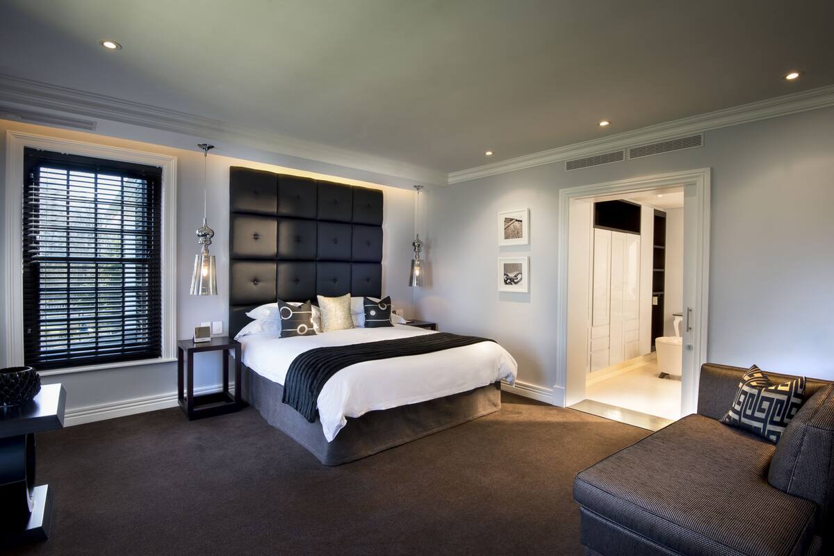 A modern bedroom with a large bed, a nightstand, a bedside table, a sofa, and a walk-in closet.