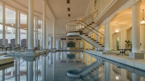 Ein großes Hallenbad mit einer zentralen Treppe, großen Fenstern und einem Balkon.