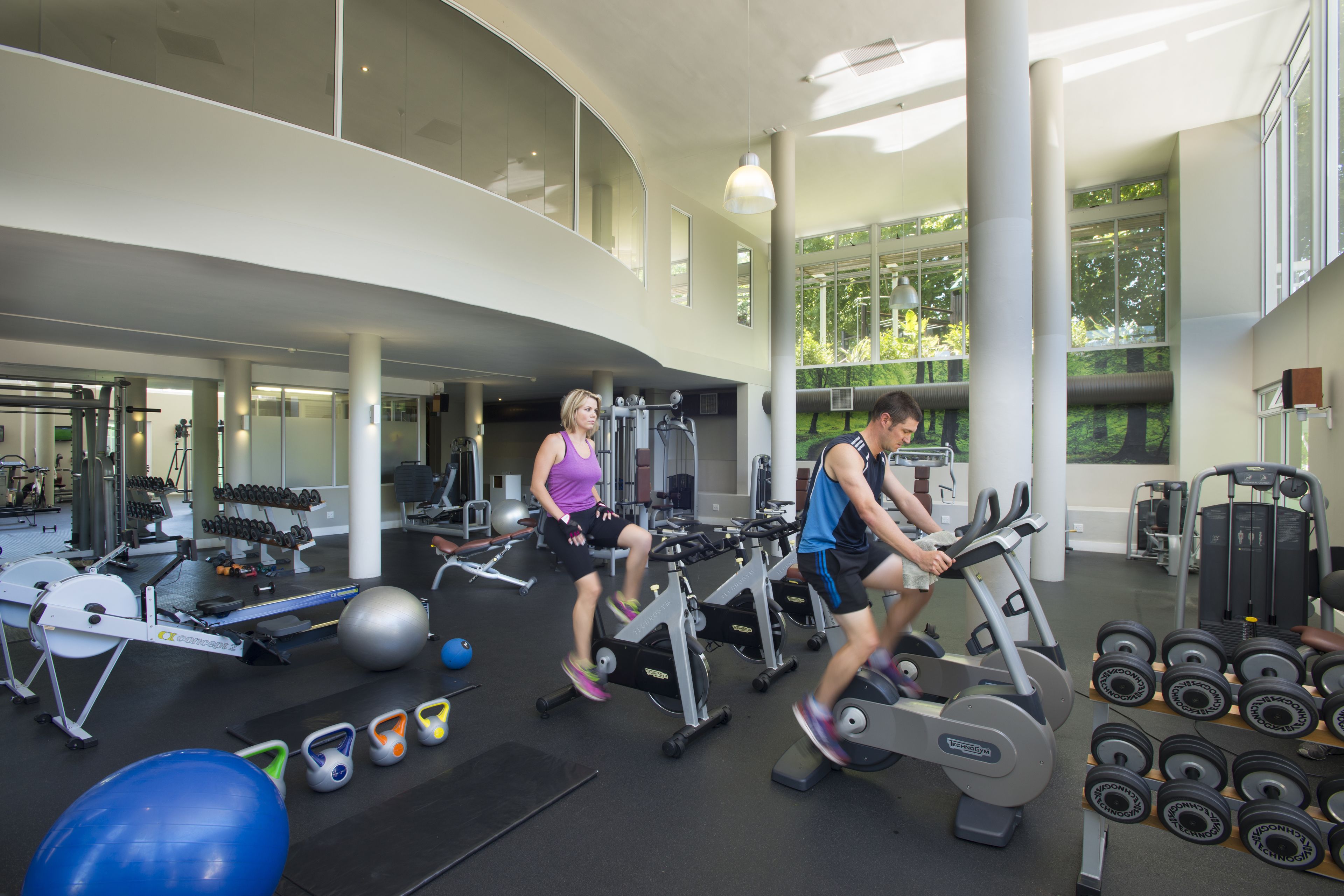 Uma academia com esteiras, halteres e bolas de exercício.