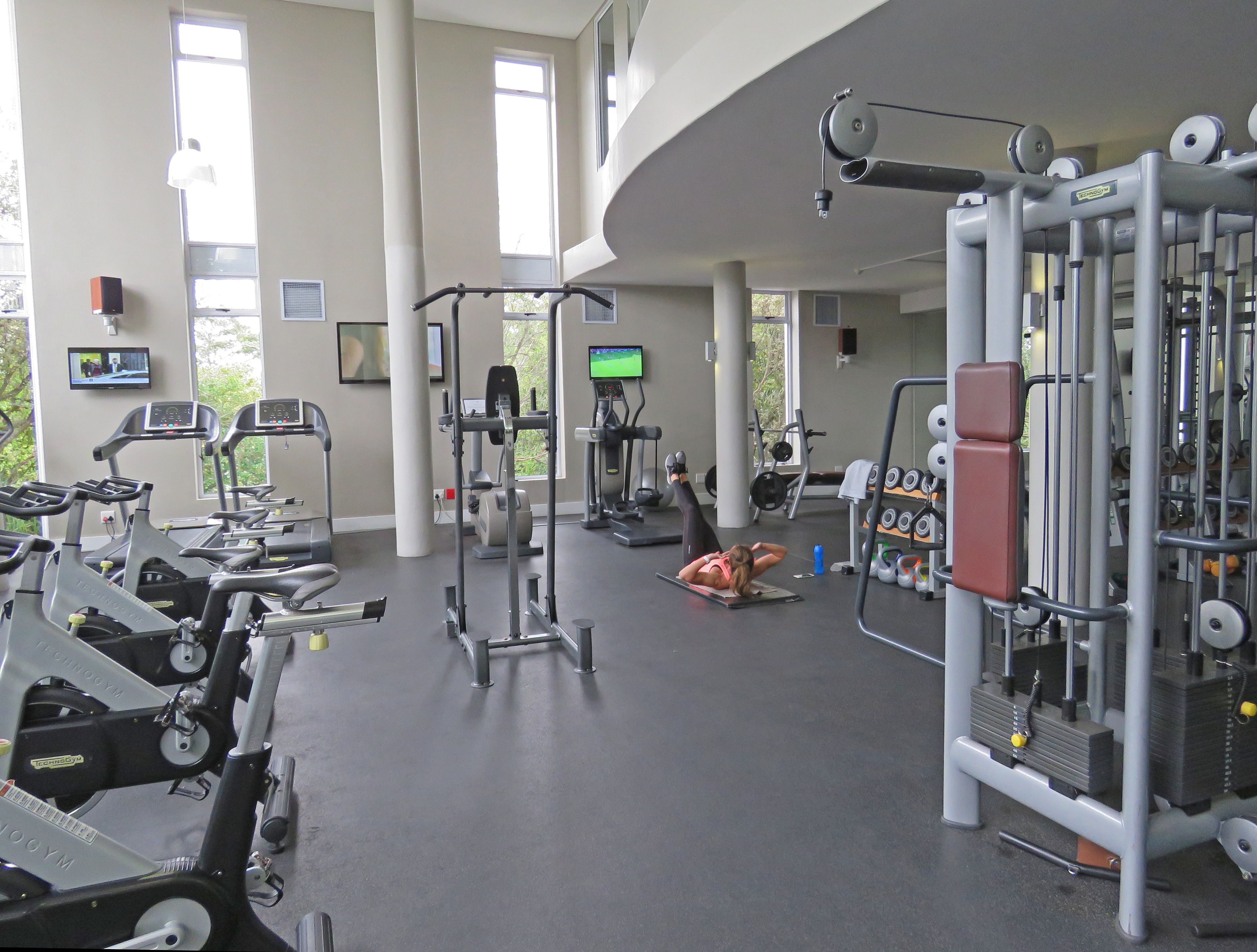 Een sportschool met diverse fitnessapparaten, waaronder loopbanden, een krachttrainingapparaat en gewichten.
