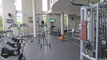 Een sportschool met diverse fitnessapparaten, waaronder loopbanden, een krachttrainingapparaat en gewichten.