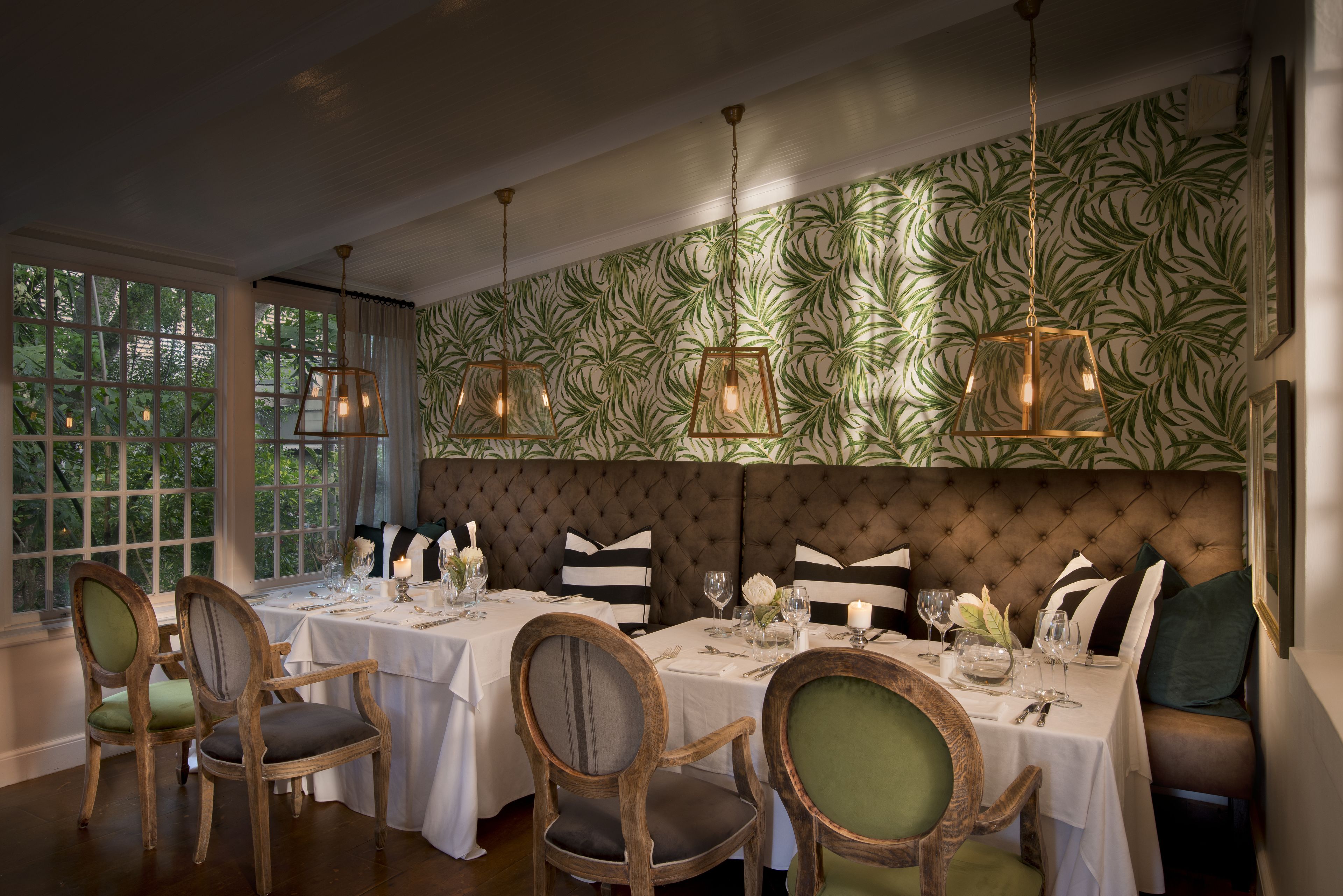 A dining area with a large window, a tufted headboard, and hanging pendant lights.
