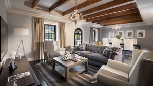 Ein geräumiges Wohnzimmer mit hoher Decke, Holzbalken, einem Chandelier, einer Sofagarnitur, einem Couchtisch und einem Fernseher.