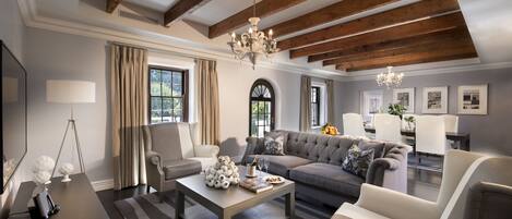 Ein geräumiges Wohnzimmer mit hoher Decke, Holzbalken, einem Chandelier, einer Sofagarnitur, einem Couchtisch und einem Fernseher.