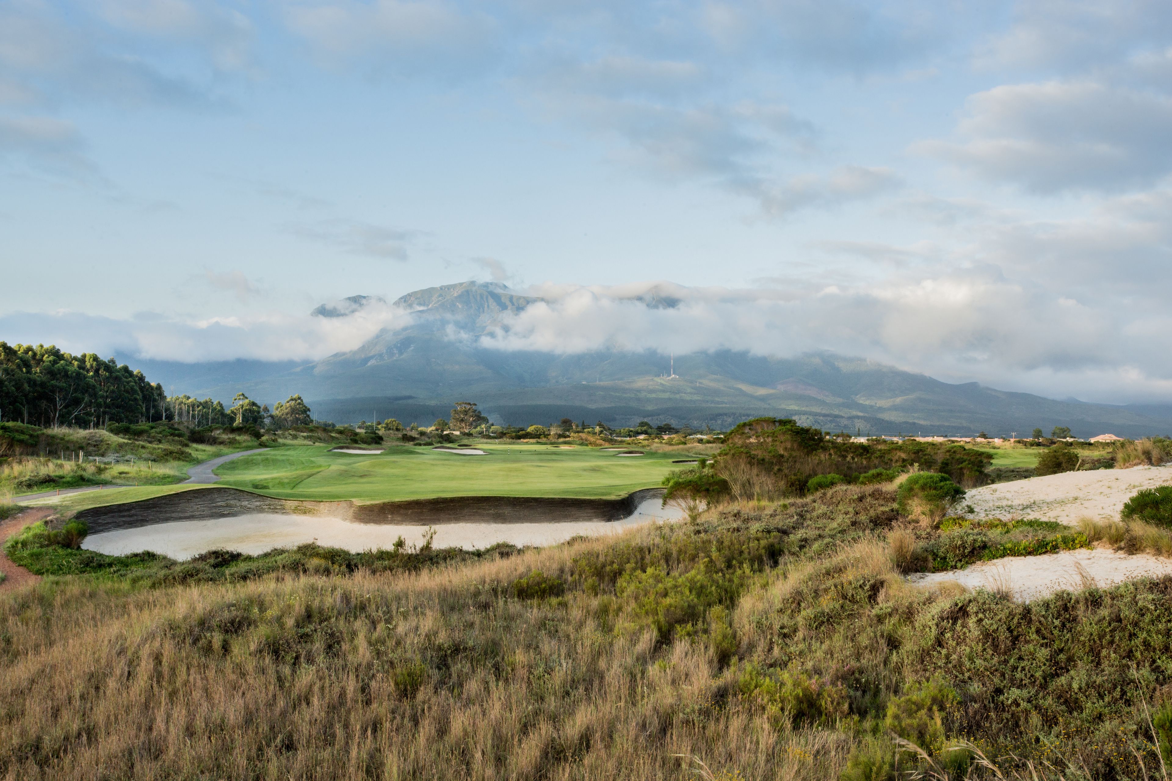 A golf course with bunkers, a water hazard, and a mountain in the background.