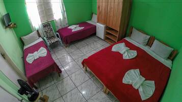 Two beds with red bedding and white towels are complemented by a wardrobe and a small refrigerator.