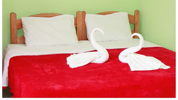 Un lit avec une couverture rouge, deux oreillers blancs et deux serviettes blanches en forme de cygne.