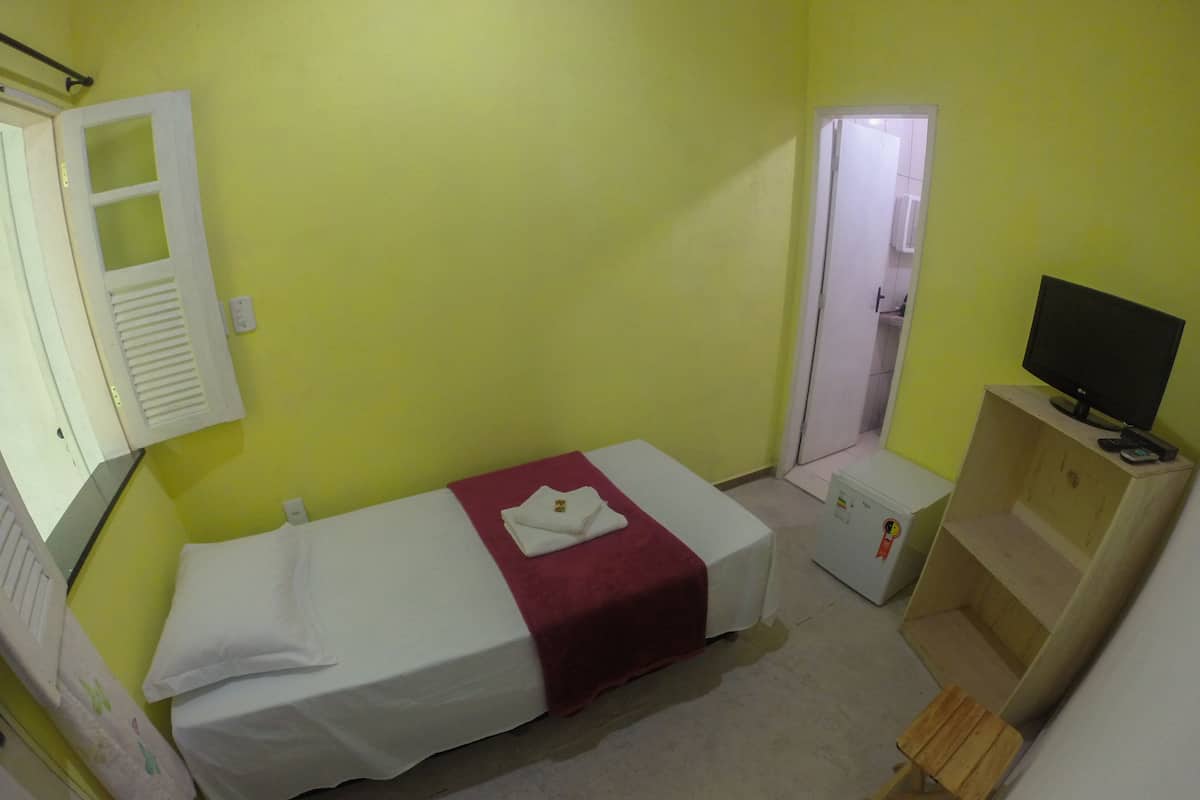 Een kleine eenpersoonskamer met een bed, een televisie, een klein houten tafeltje en een deur naar een badkamer.