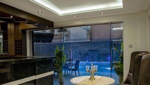 A modern interior with a dining area featuring a marble table and a candelabra, a leather sofa, and a view of a backyard with a pool. - The Landmark Suites Westlands, Nairobi- Next to Westgate Mall (Nairobi)