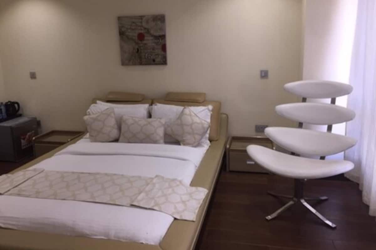 A hotel room with a bed, a chair, a small table, and a painting on the wall.