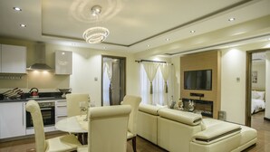 A modern living room with a sofa, dining table, and chairs. There is a TV mounted on the wall and a fireplace. - The Landmark Suites Westlands, Nairobi- Next to Westgate Mall (Nairobi)
