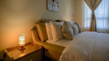 A neatly made bed with white linens, a bedside table with a lamp, and a wall-mounted artwork.