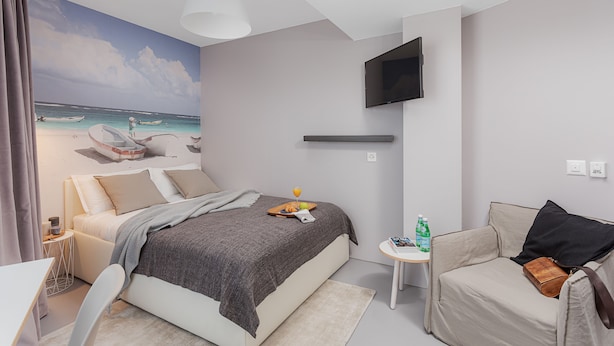 A modern hotel room with a bed, a sofa, a TV, and a mural of a beach scene. - VISIONAPARTMENTS Lucerne Neustadtstrasse (Lucerne)