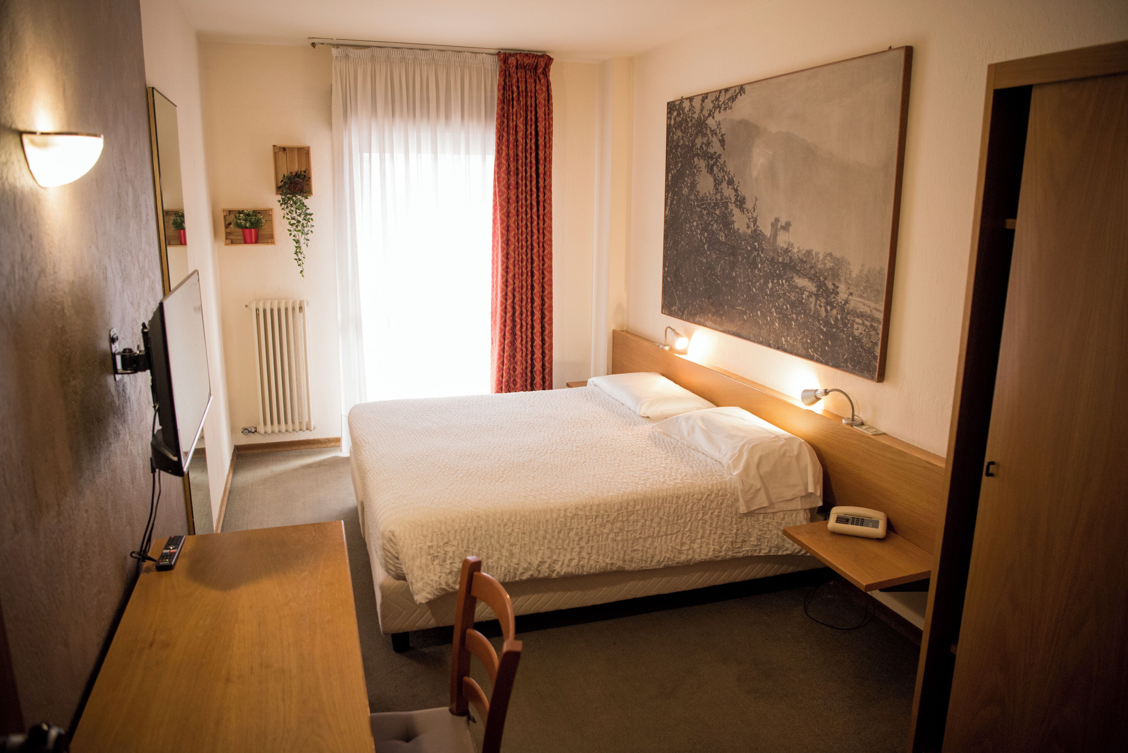 A hotel room with a bed, bedside table, lamp, chair, and a large painting on the wall.
