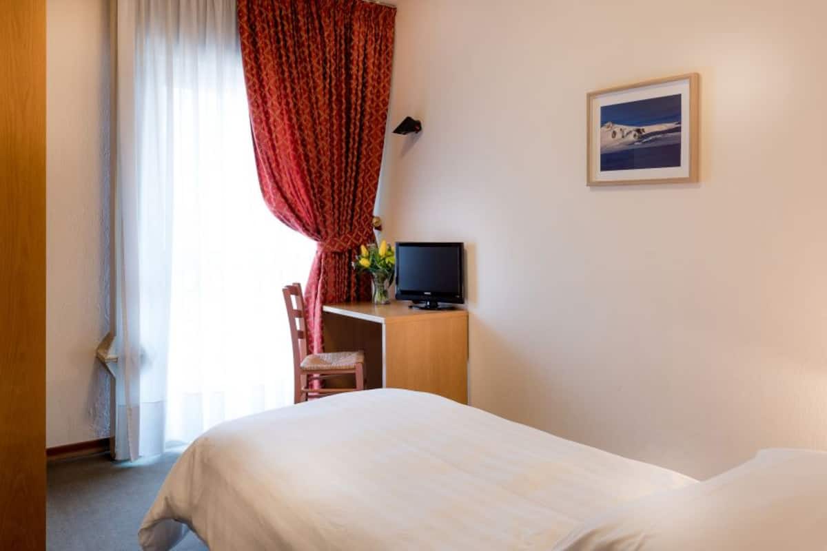 Habitación de hotel con cama, escritorio con televisor, silla y ventana con cortinas.