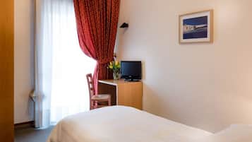 Une chambre d’hôtel avec un lit, un bureau avec une télévision, une chaise et une fenêtre avec des rideaux.