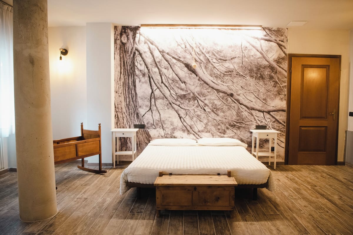 Un dormitorio con una cama grande, un banco de madera, mesitas de noche y un mural de mármol.