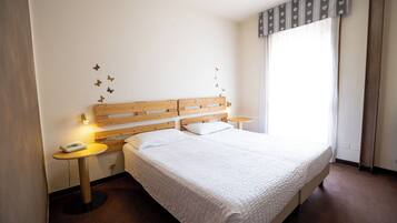 A bedroom with a wooden headboard, a single bed, two bedside tables, a wall-mounted phone, and a window with curtains.