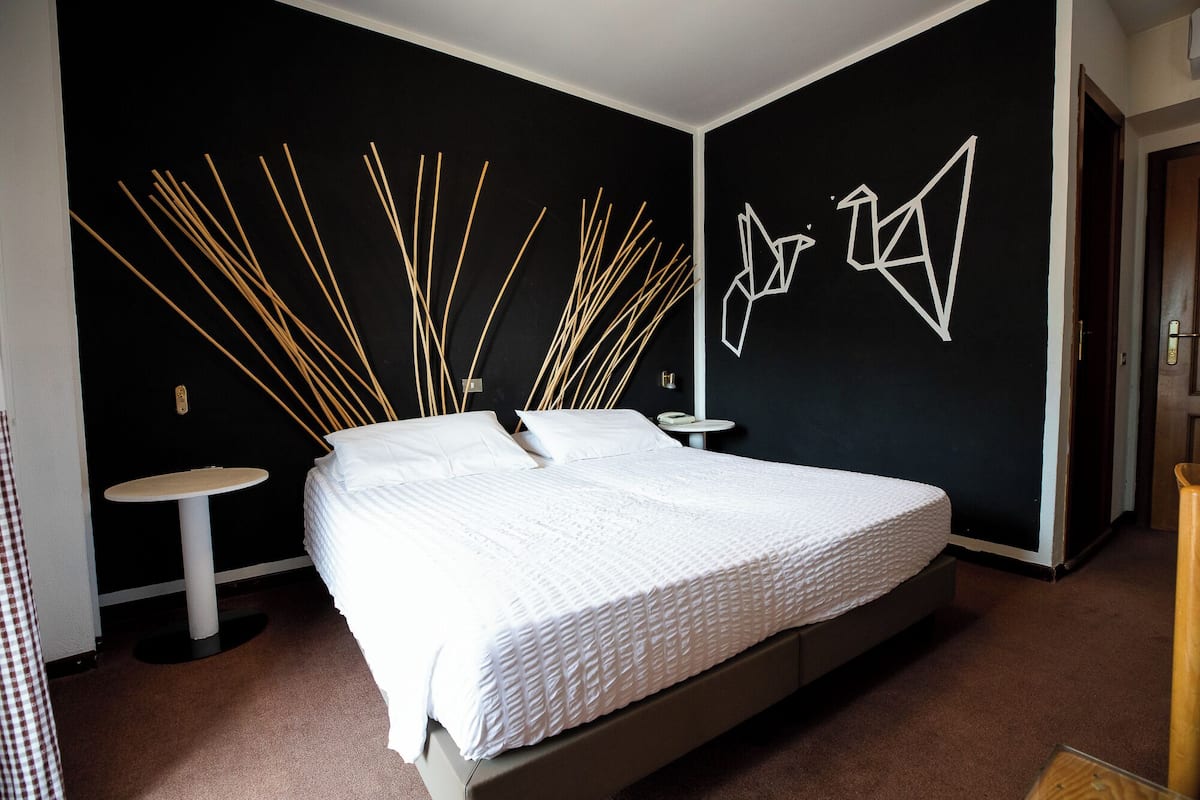 Un dormitorio moderno con una cama grande, una mesita de noche pequeña y un espejo adosado a la pared.