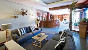 A modern hotel lobby with a dark-colored sofa, a wooden coffee table, and a reception desk in the background. - Hotel Rendez Vous (Chatillon)