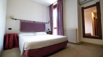 Un dormitorio con una cama, una mesita de noche, una ventana con cortinas, un radiador y un espejo en la pared.