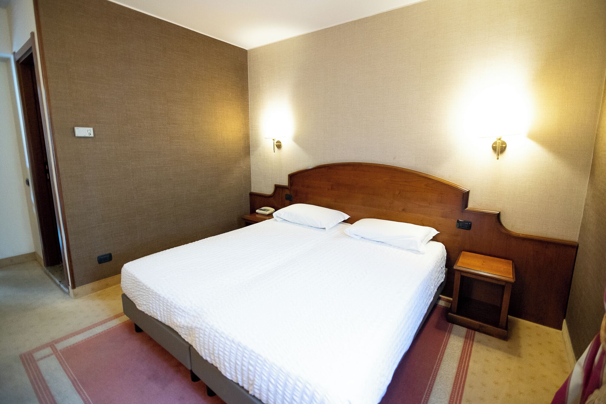 A hotel room with a large bed, two bedside tables, and two wall-mounted lamps.