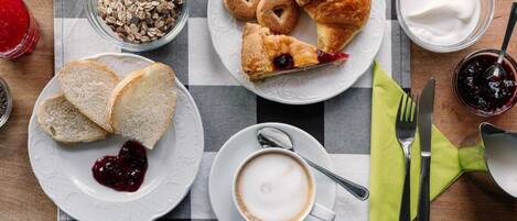 Un desayuno con cruasanes, pan, mermelada, yogur y café sobre un mantel a cuadros.