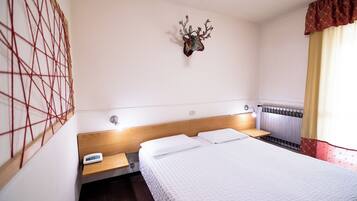 A hotel room with a bed, bedside tables, a wall-mounted phone, a radiator, and a decorative deer head on the wall.