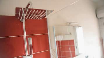 Un baño con pared de azulejos rojos, un cabezal de ducha cromado y un espejo que refleja parte del cuarto.