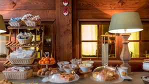 A breakfast buffet with various food items and baskets, a lamp, and a window with warm lighting. - Hotel Rendez Vous (Chatillon)