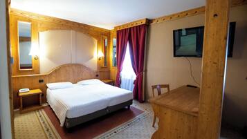 Habitación de hotel con cama, mesita de noche, lámpara, espejo, televisor y escritorio de madera.