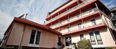 A multi-story building with a red roof, balconies, and a staircase leading to the entrance.