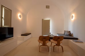 Una habitación moderna con una televisión, dos sillas de madera, un sofá y una mesa de comedor.