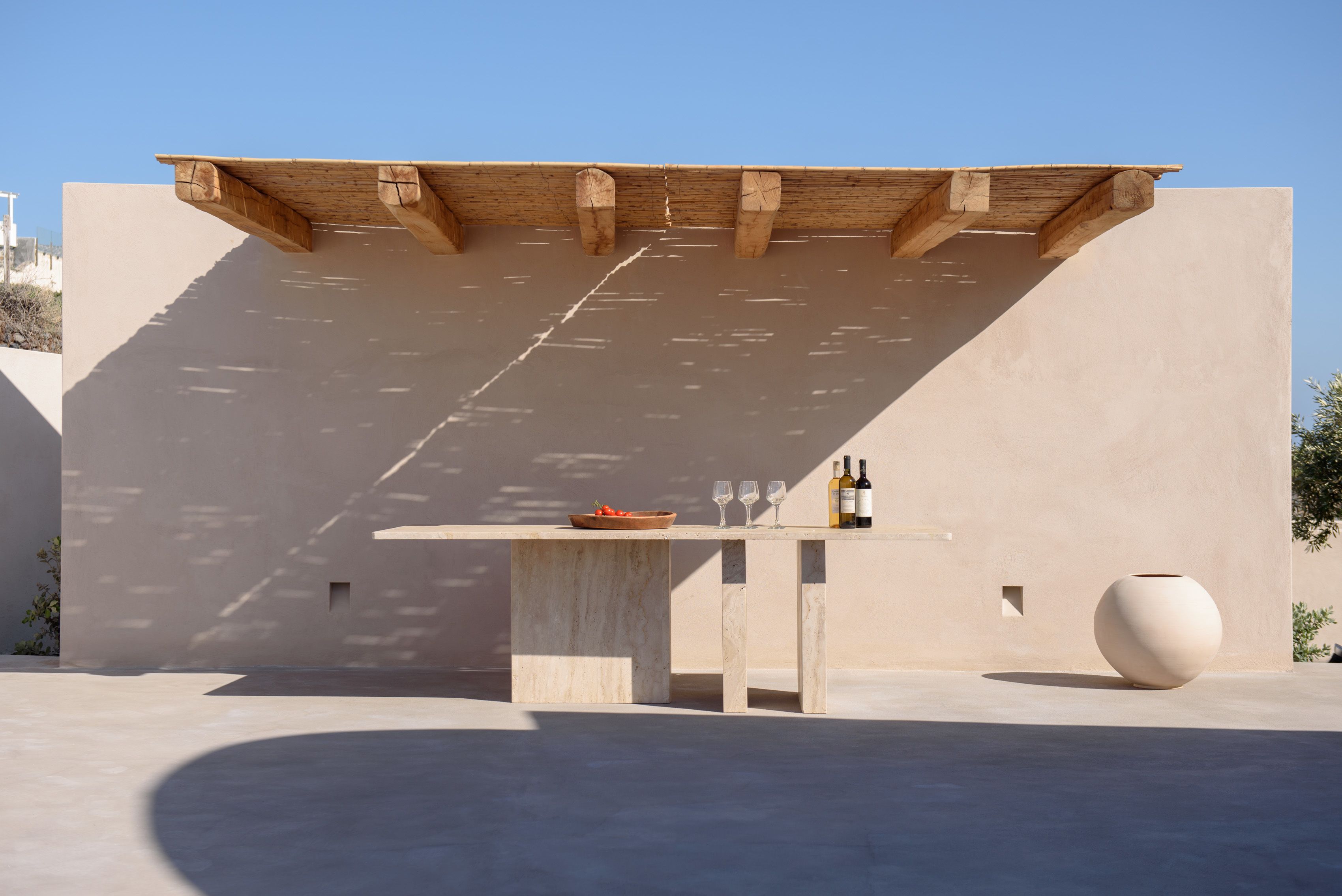Un patio extérieur au design minimaliste, agrémenté d’une pergola en bois, d’une table en béton et d’un grand vase.