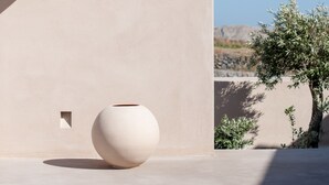 Disseny arquitectònic minimalista amb un vas blanc gran i una biga de fusta davant d'una paret sense adorns.