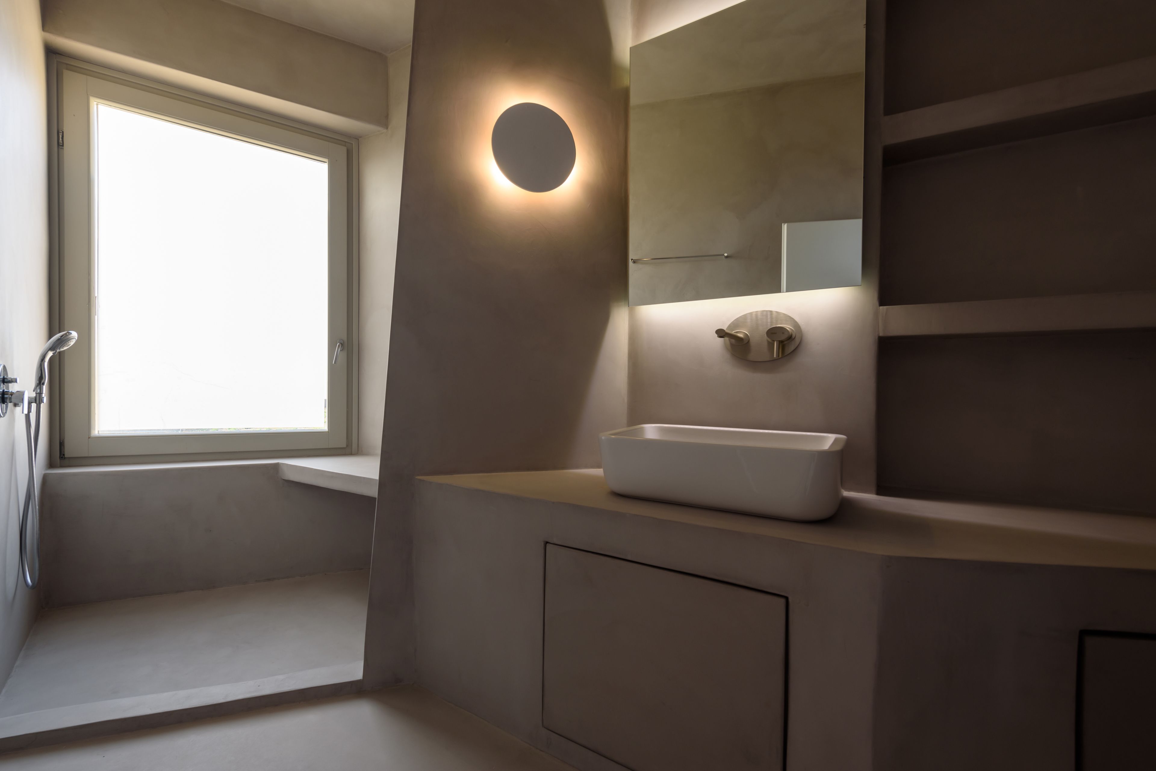 A modern bathroom with a built-in window, a round mirror, and a white basin.
