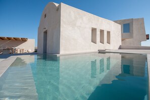 Un edificio moderno con piscina, que destaca por su diseño arquitectónico único, grandes ventanales y un cielo azul despejado.