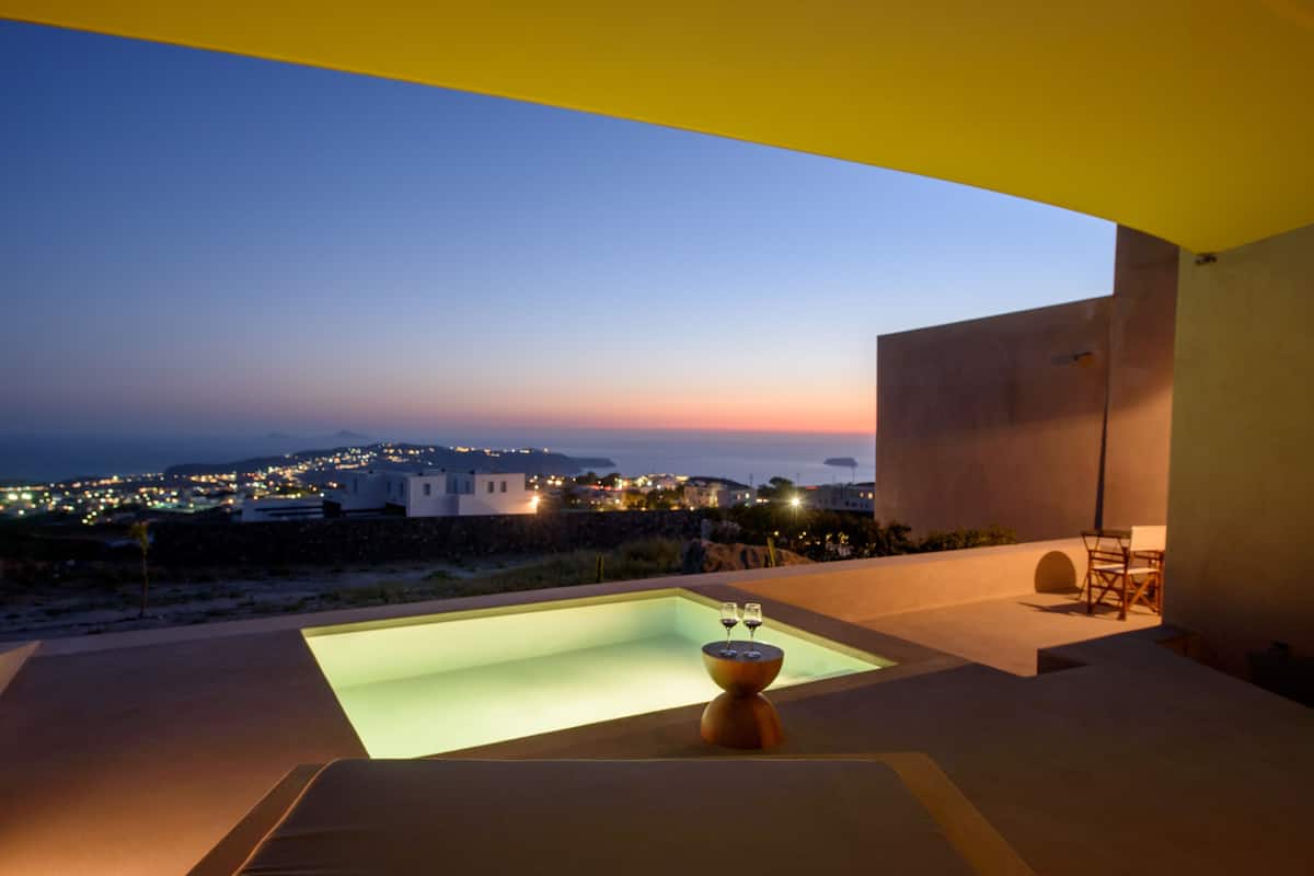 A modern outdoor pool area with a view of a coastal town at dusk.