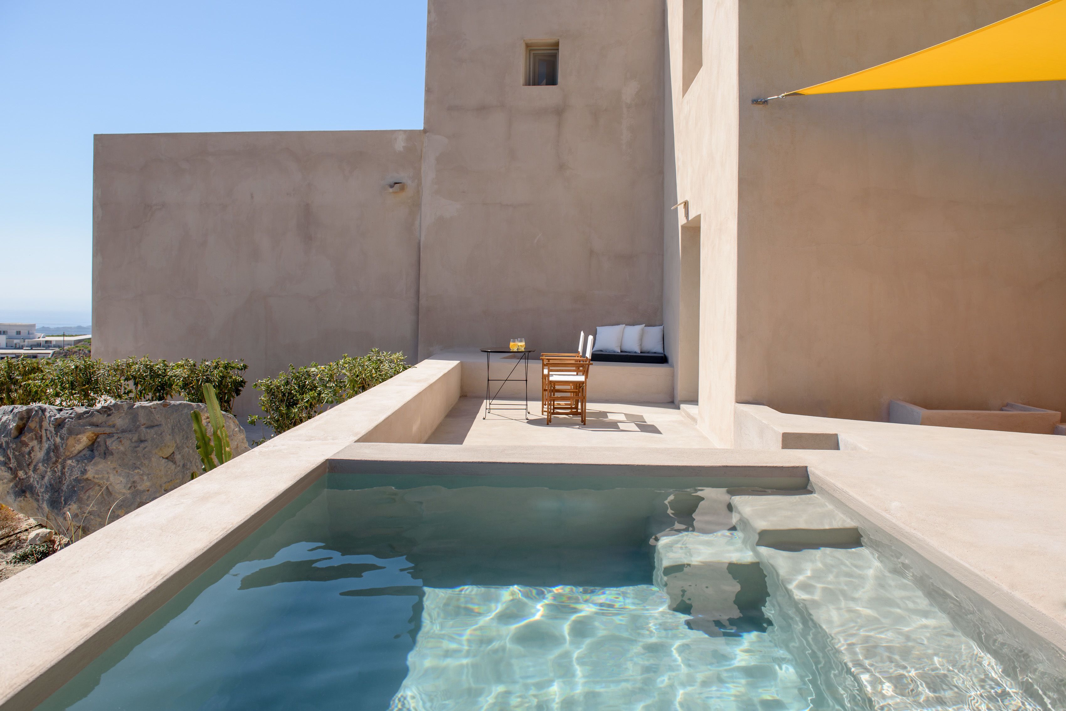 A rooftop pool area with a clear view of the cityscape, a seating area with a table and chairs, and a small window.