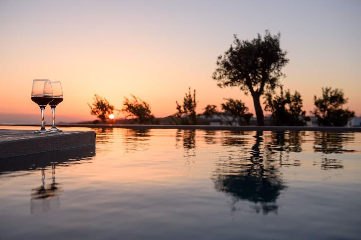 A sunset over a calm body of water with two glasses of red wine on a table.