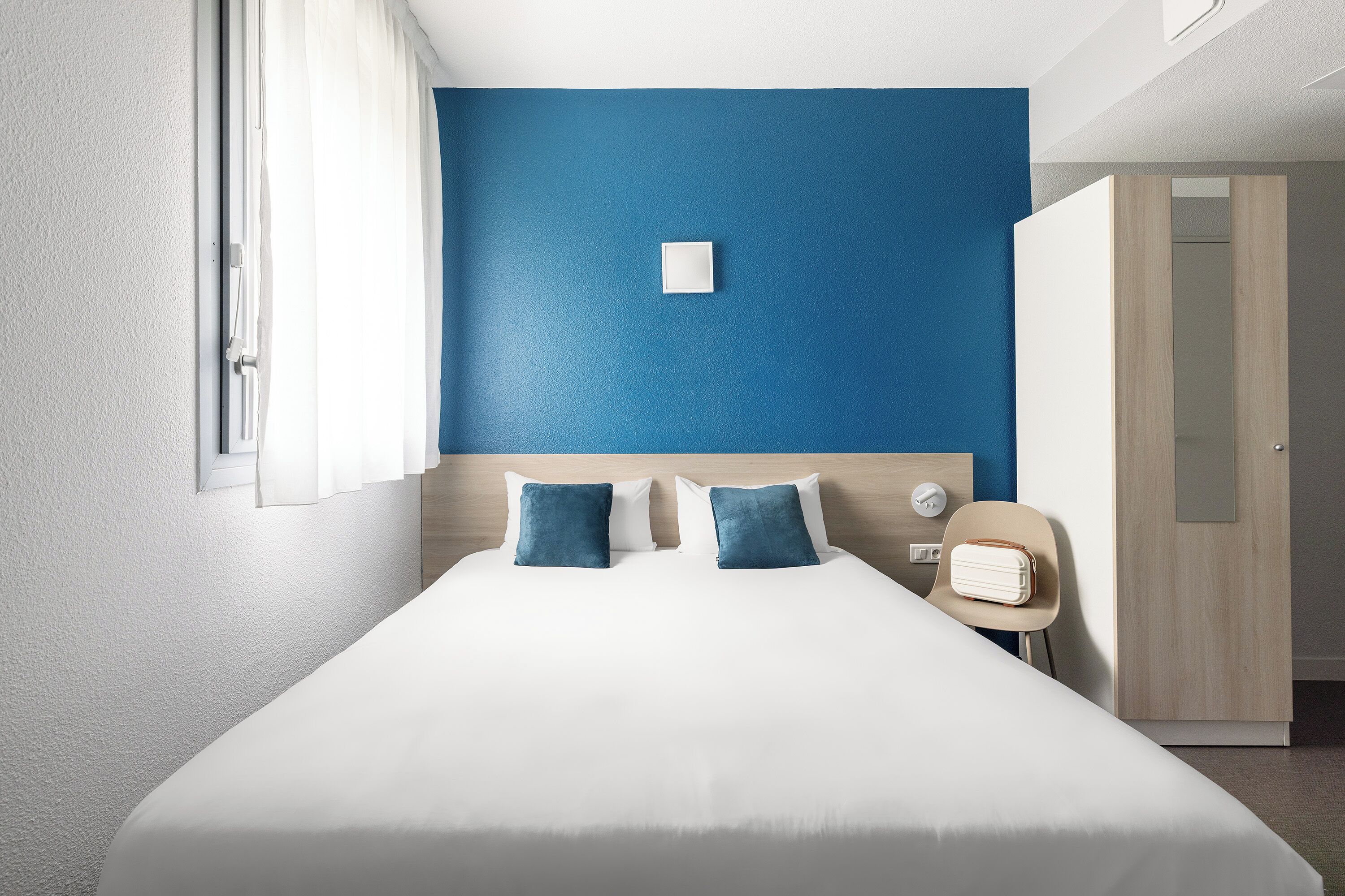 A hotel room with a large bed, two pillows, a bedside table, a chair, and a wardrobe.