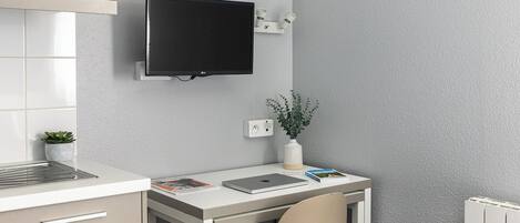 A modern kitchen with a microwave, a flat-screen TV mounted on the wall, a small potted plant, and a desk with a chair.