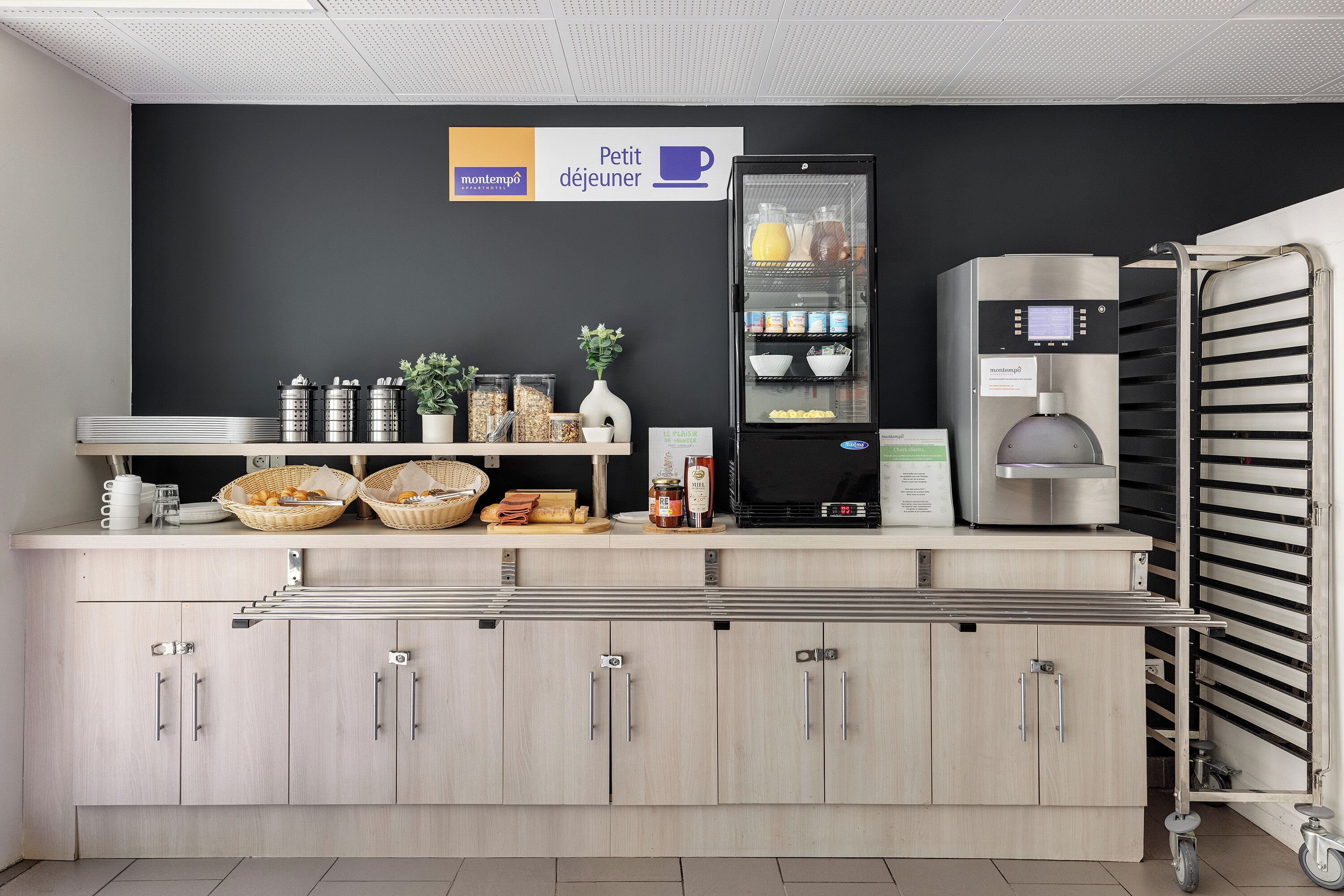 Une petite cuisine équipée d’une machine à café, d’un réfrigérateur et de divers produits alimentaires disposés sur le plan de travail.