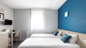Een hotelkamer met twee bedden, een bureau, een stoel, een televisie en een raam met gordijnen.