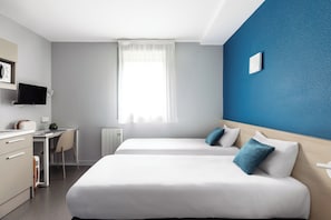 Une chambre d’hôtel avec deux lits, un bureau, une chaise, une télévision et une fenêtre avec des rideaux.