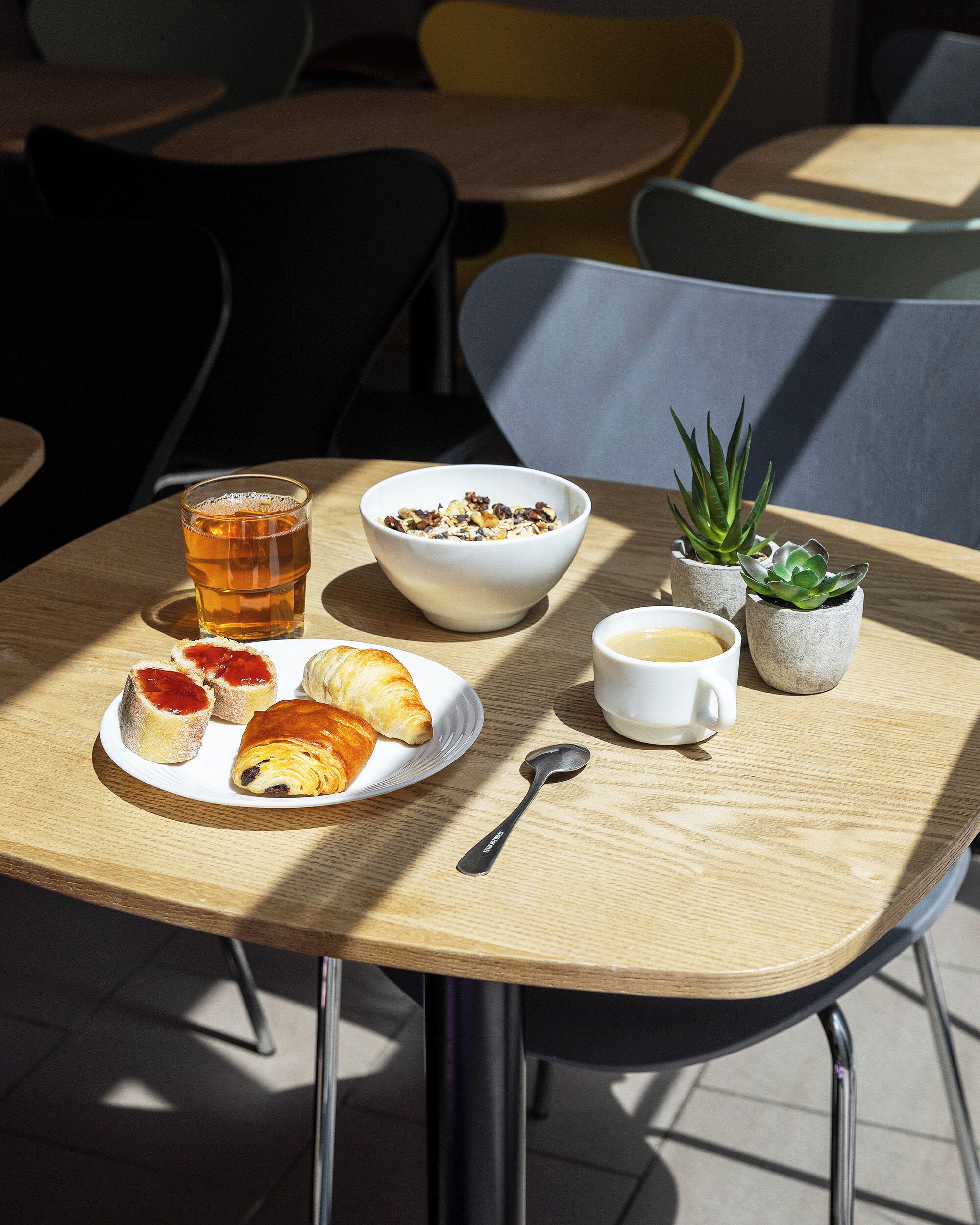 Una mesa con un tazón de cereal, una taza de té, un plato de pasteles, una taza de café y una pequeña planta en maceta.
