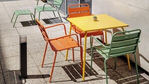 Een terras met een tafel en stoelen, een raam en een betonnen muur.